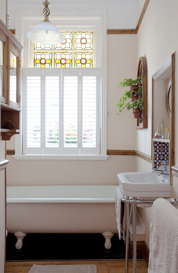 Sonnendurchflutetes Badezimmer mit originalen Buntglasfenstern, Waschtisch und freistehender Badewanne in einem Stadthaus in London, England, Vereinigtes Königreich