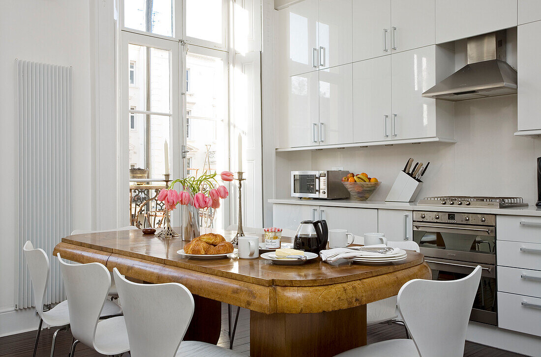 Antique table in white kitchen set for breakfast in London townhouse