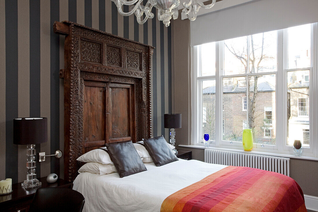 Gestreifte Tapete und geschnitztes Holzkopfteil im Schlafzimmer eines Londoner Stadthauses
