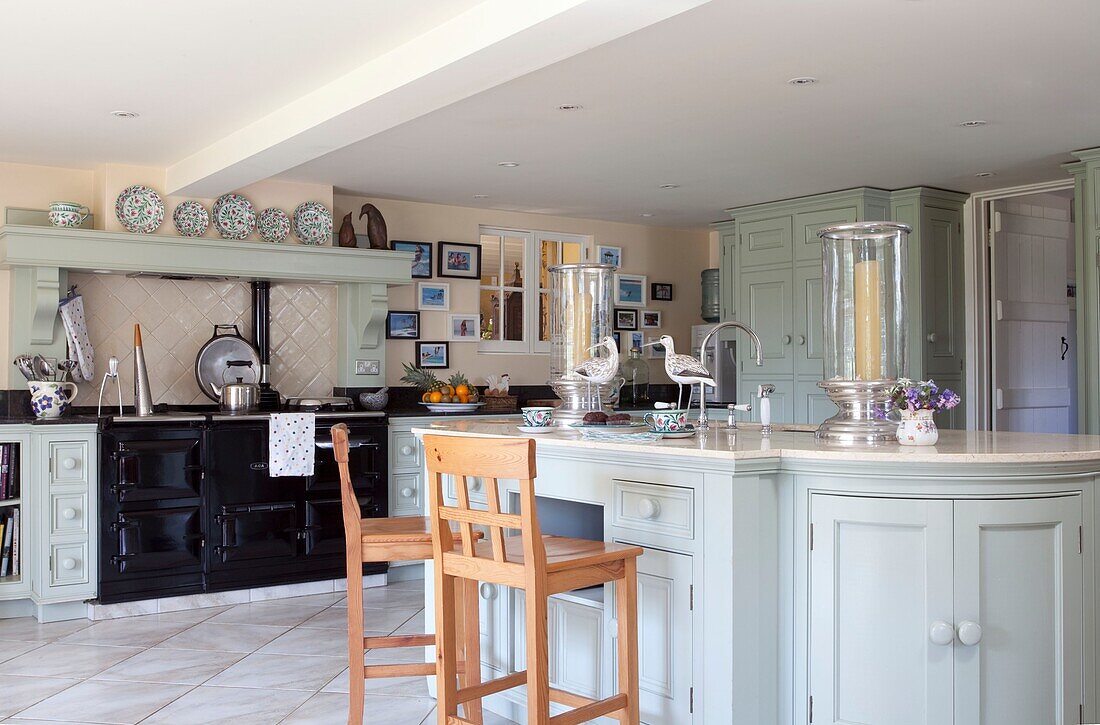 Wooden barstools at breakfast bar in pastel green kitchen with range oven, Kent, England, UK