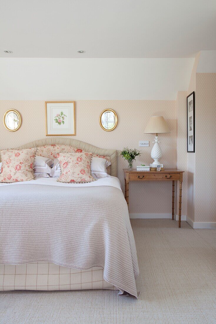 Floral cushions on bed with wooden bedside table in Kent cottage, England, UK