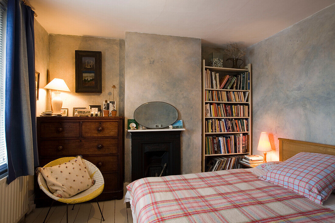 Beleuchtete Lampen im Schlafzimmer eines Hauses in Rye mit Bücherregal und karierter Decke, East Sussex, England, UK