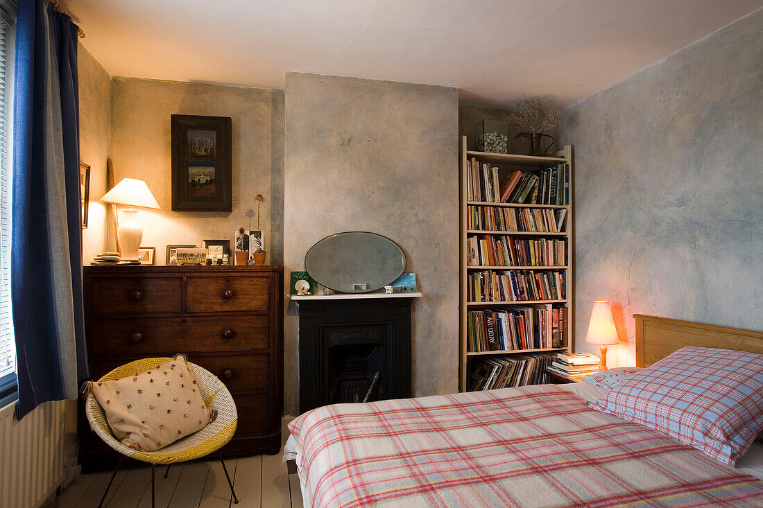 Lit lamps in bedroom of Rye home with bookcase and checked blanket, East Sussex, England, UK