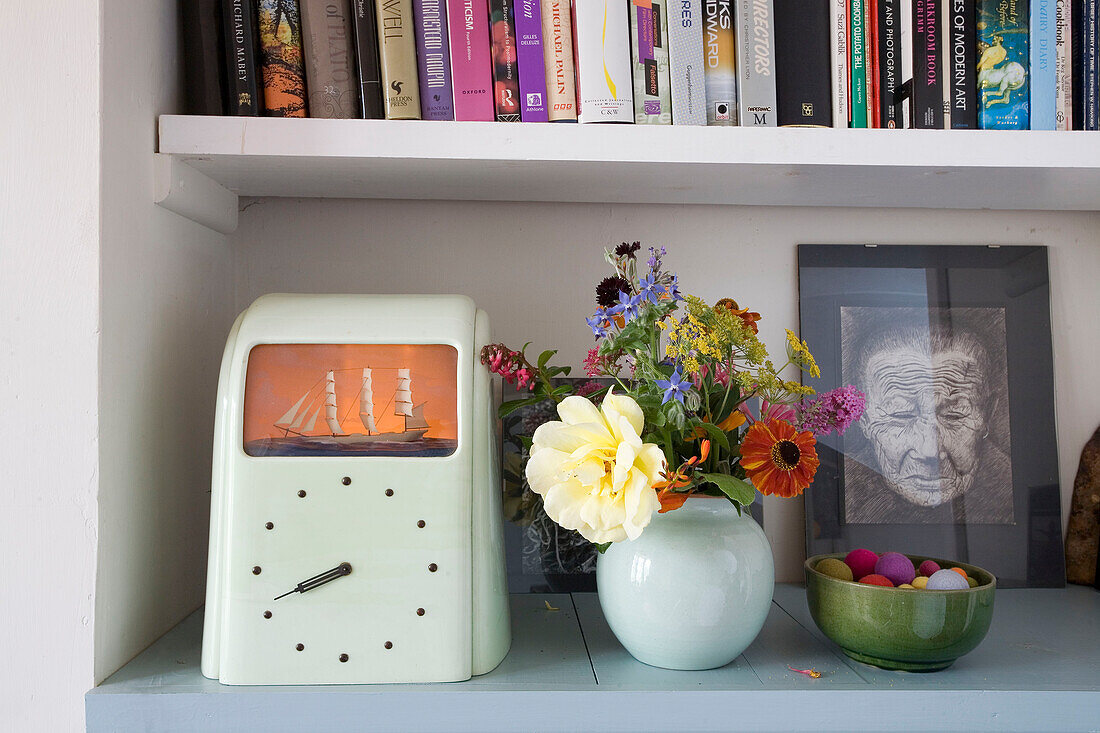 Nautische Uhr und geschnittene Wildblumen mit Bücherregal im Haus in Rye, East Sussex, England, UK