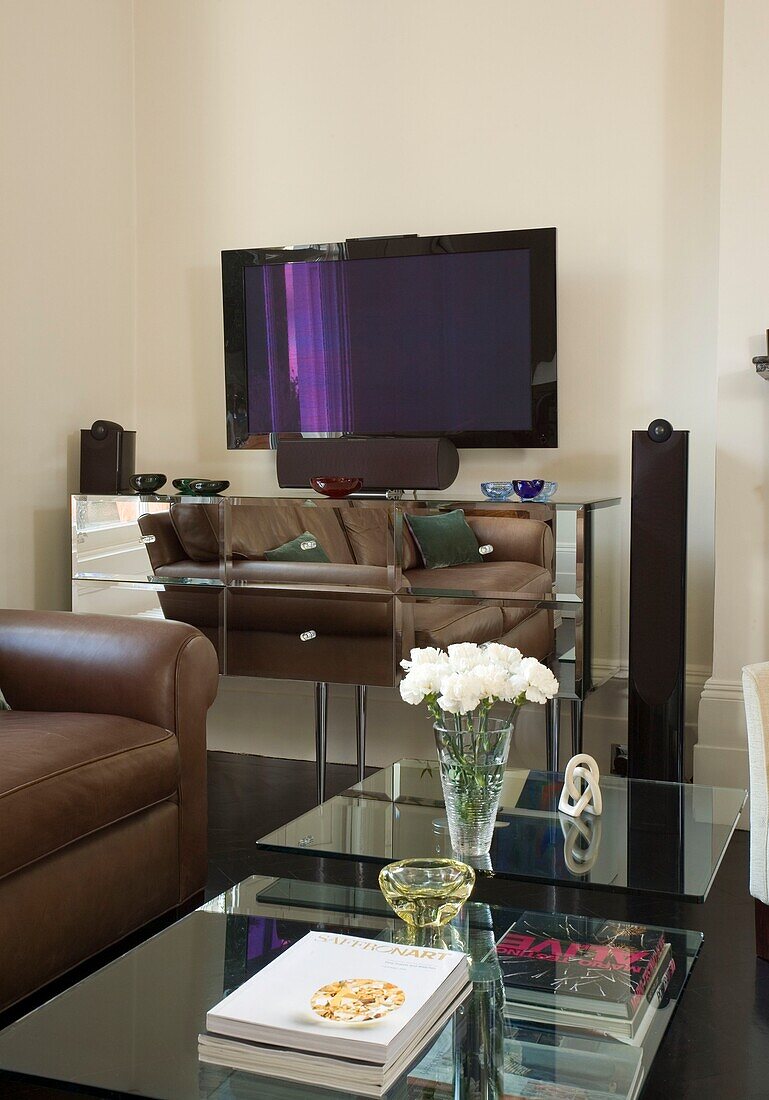 Brown leather sofa reflected in mirrored sideboard with plasma screen London UK