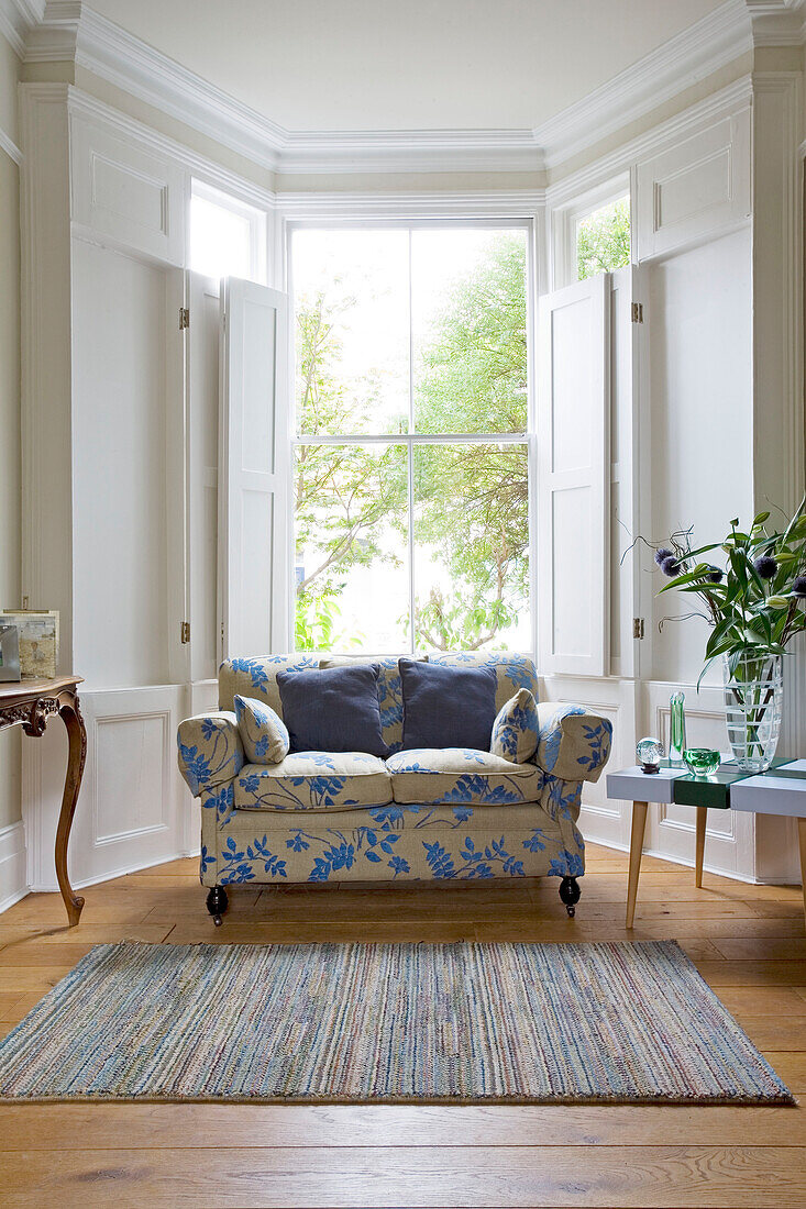Floral gemustertes Zweisitzer-Sofa in einem Erkerfenster mit Fensterläden in einem Haus in London, England, UK