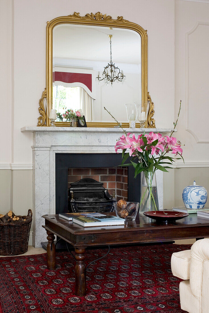 Cut lilies on wooden coffee table in front of fireplace with gilt mirror in classic Tyne & Wear home, England, UK