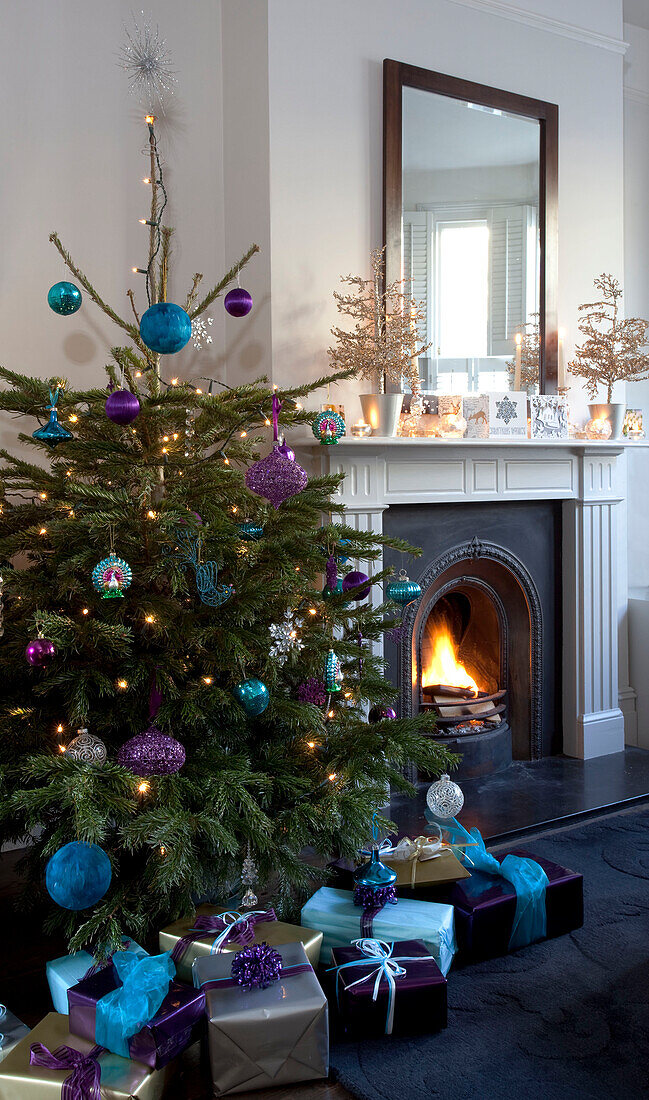 Geschenke unter dem Weihnachtsbaum neben dem beleuchteten Feuer in einem Haus in London, UK
