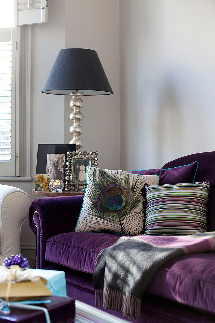 Pfauenfeder und gestreiftes Kissen auf lilafarbenem Sofa in einem modernen Haus in London, UK