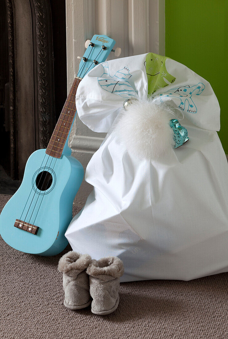 Hellblaue Gitarre und Sack mit Weihnachtsgeschenken auf dem Boden mit Hausschuhen in einem modernen Londoner Haus, UK