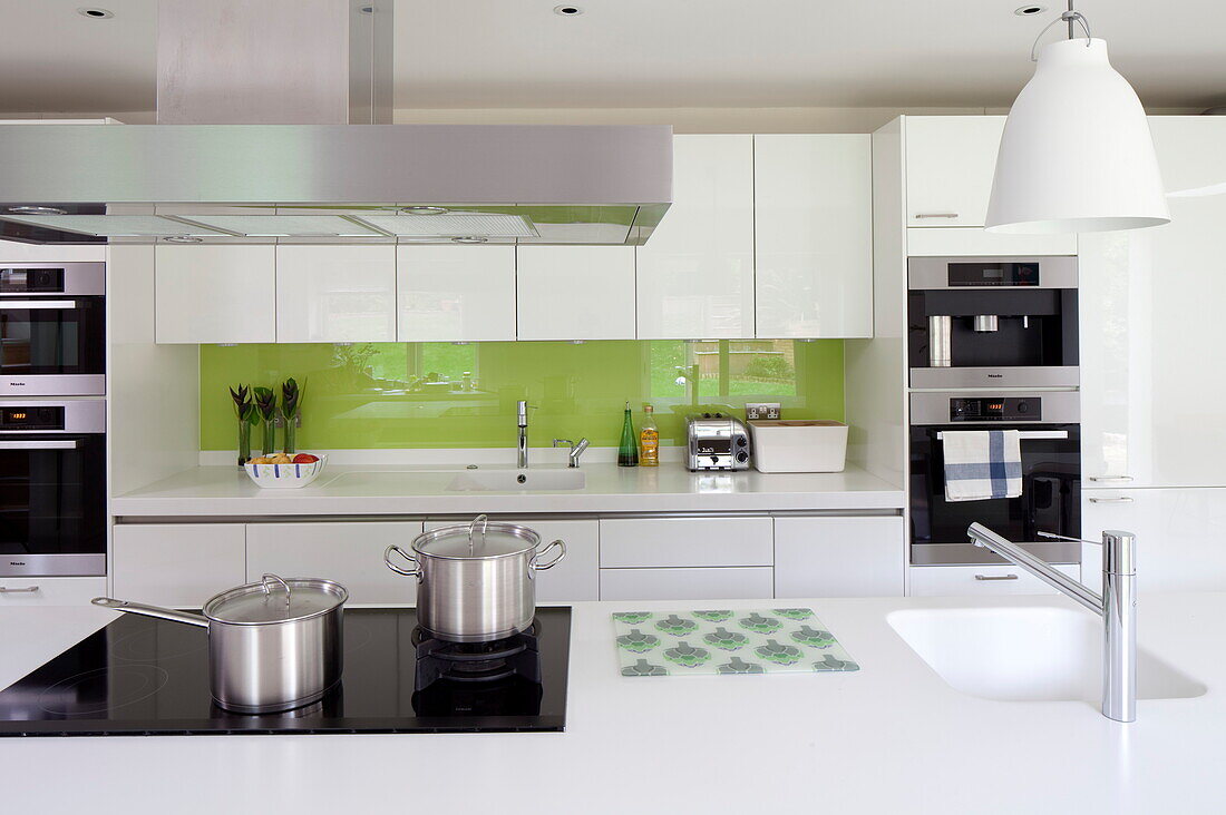 Metal pans on electric hob in kitchen with with lime green splashback in contemporary London home, England, UK