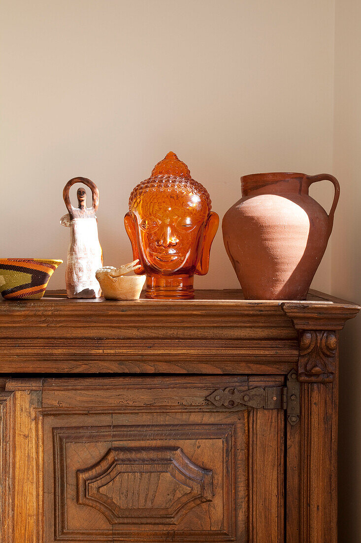 Töpferkrug und Buddhakopf auf geschnitztem Holzschrank in einem Londoner Haus, UK