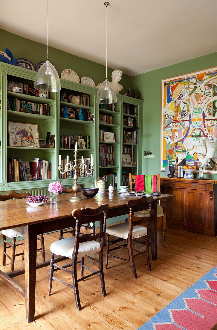 Wooden dining table and chairs with green painted bookcase in London home England UK