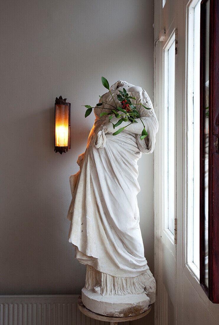 Headless statue with Christmas holly and lit wall lamp in London home, England, UK