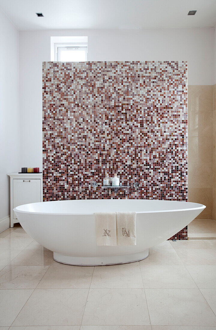 Freestanding bath with mosaic tiled partition in contemporary bathroom of London home, UK