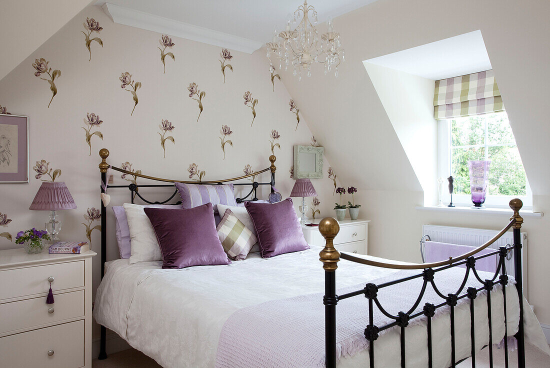 Brass bed in floral wallpapered contemporary attic bedroom of Kent cottage, England, UK