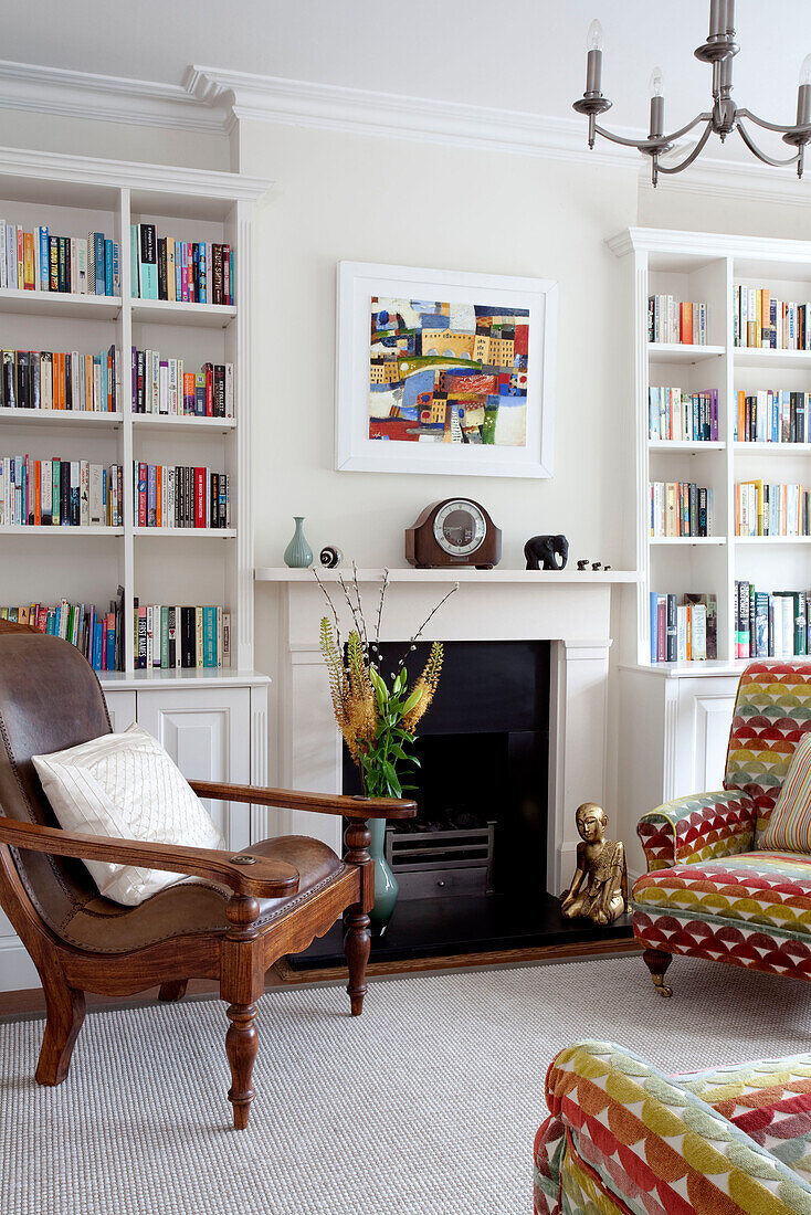 Moderne Kunst über dem Kamin mit Bücherregal und antikem Stuhl in einem Einfamilienhaus in Herefordshire England UK