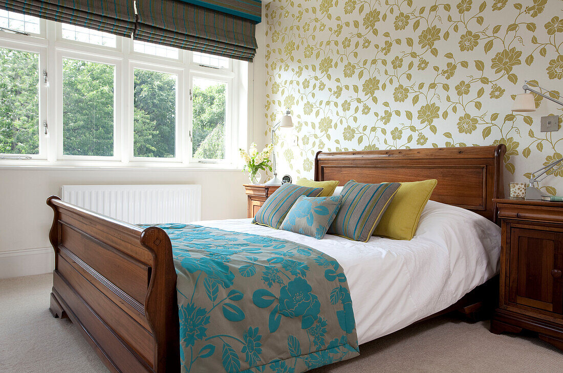 Floral quilt and patterned wallpaper with antique sleigh bed in Herefordshire family home England UK
