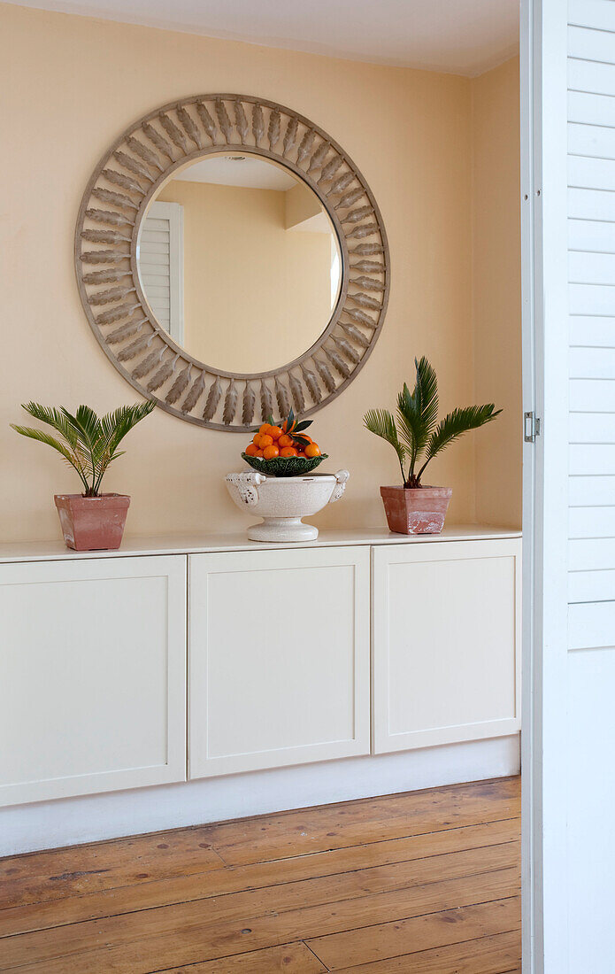 Circular mirror above side cupboard with houseplants in London home, UK