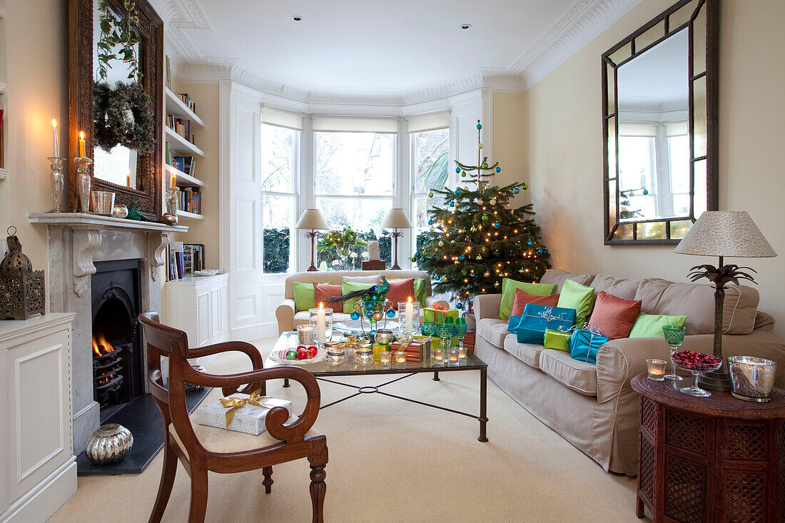 Beleuchtete Kerzen und Weihnachtsgeschenke mit Baum in Londoner Wohnzimmer mit beleuchtetem Feuer, UK