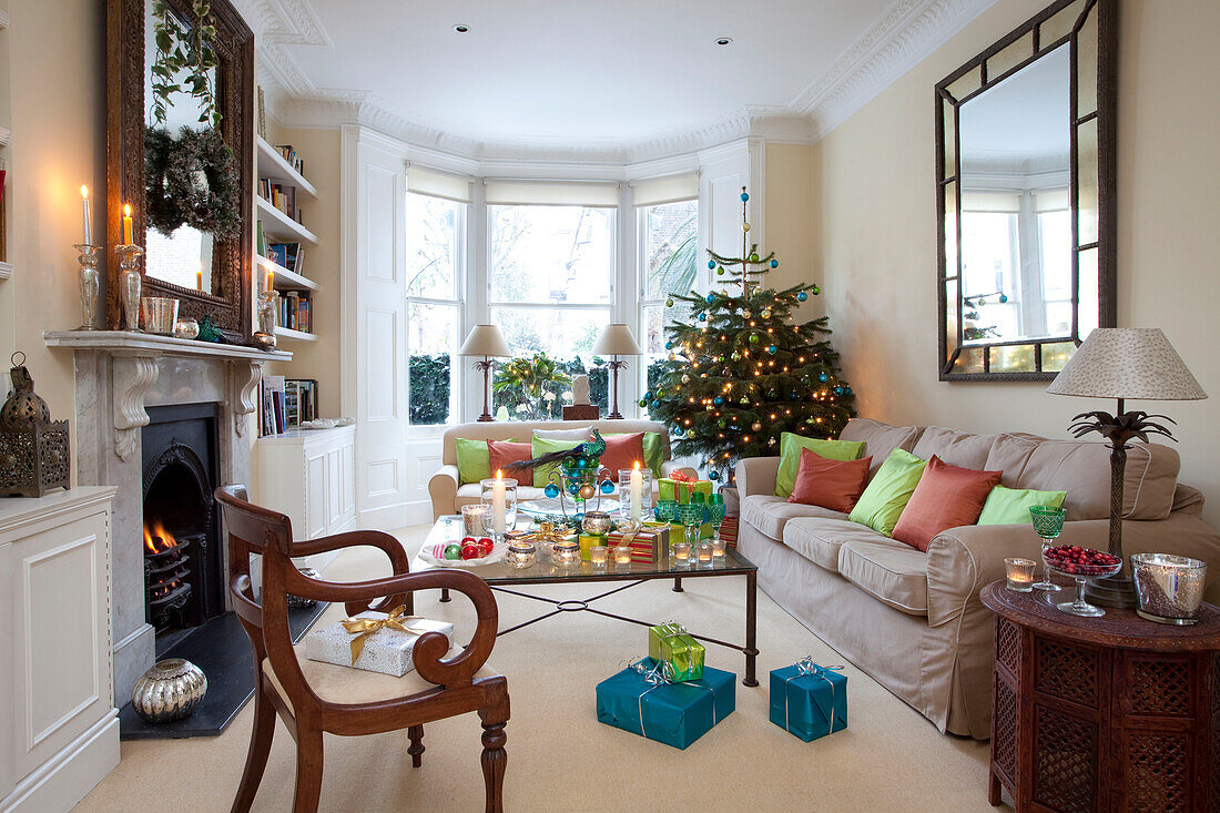 Lit candles and Christmas presents with tree in London living room with lit fire, UK