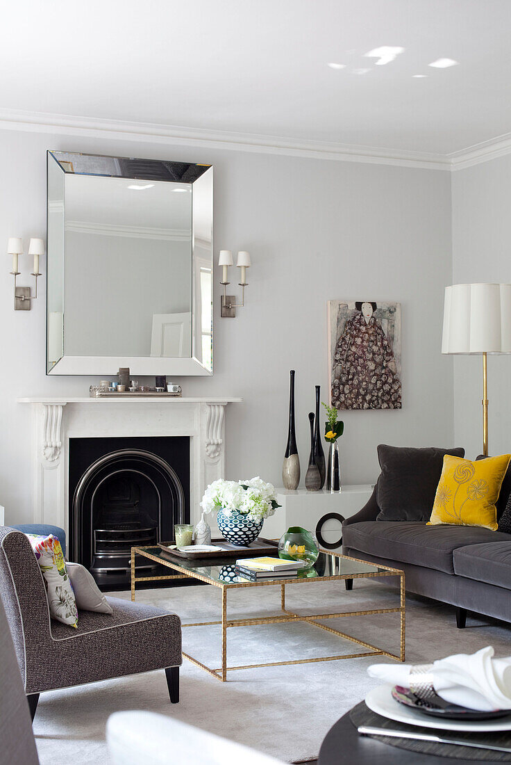 Mirror above fireplace in living room with glass topped coffee table, London apartment, UK