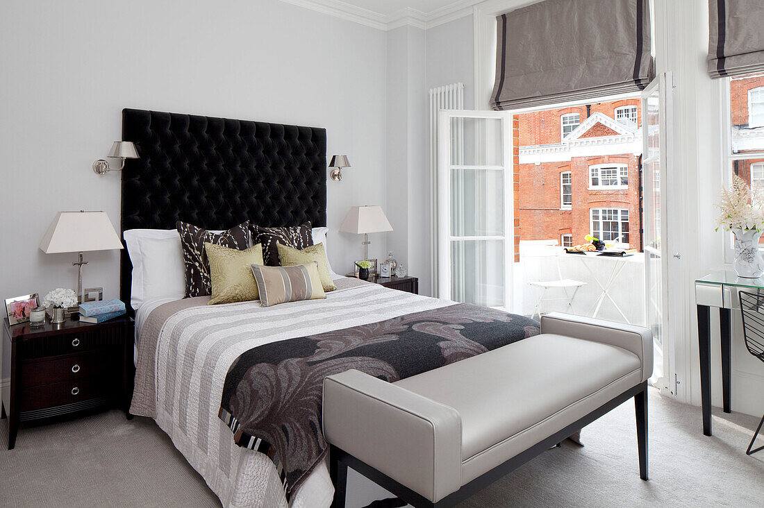 Bett mit schwarzem Kopfteil mit Knöpfen in einem Zimmer mit offenen Türen zum Balkon, Londoner Wohnung, UK