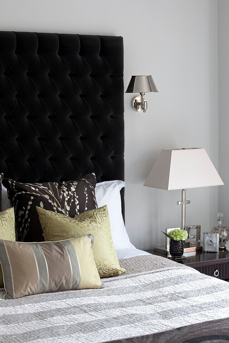 Assorted cushions on double bed with black buttoned headboard in London apartment, UK
