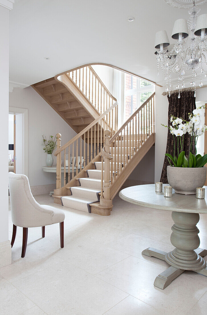 Orchid on pedestal base table with pale wood staircase in entrance hallway of contemporary Surrey country home England UK