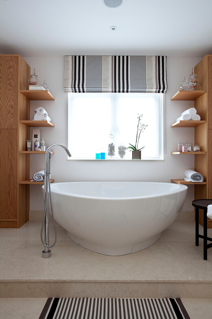 Regal aus hellem Holz mit moderner freistehender Badewanne in einem Landhaus in Surrey, England, UK