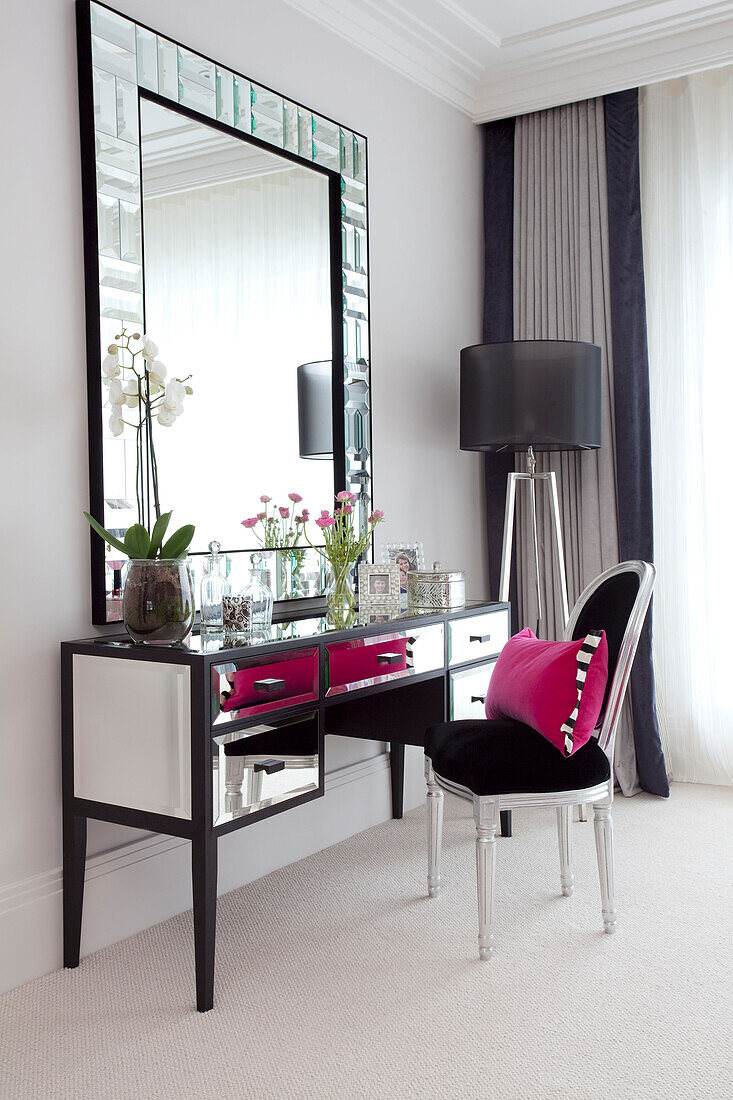 Schwarzer Stuhl mit rosa Kissen am verspiegelten Schminktisch mit großem Spiegel im Schlafzimmer eines modernen Landhauses in Surrey, England UK