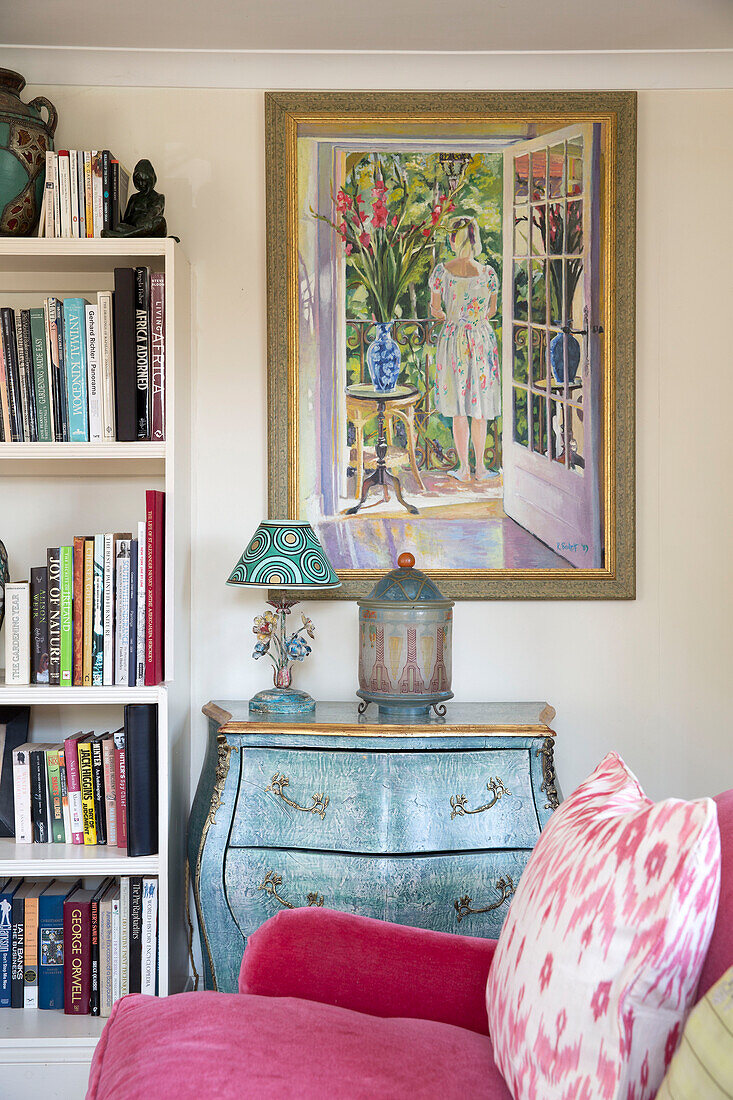 Colourful artwork above painted side unit with bookcase in living room of Sussex home England UK