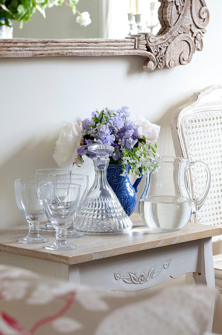 Jug of water and glasses on side table with cut flowers in Sussex cottage, England, UK