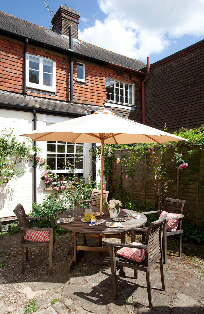 Gartentisch und Stühle im Schatten eines Sonnenschirms im Garten eines Landhauses in Sussex, England, UK