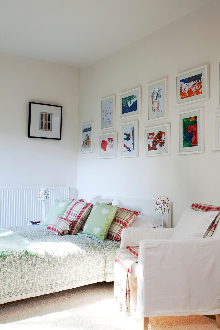 Sunlit bed and armchair with artwork in contemporary London townhouse, England, UK