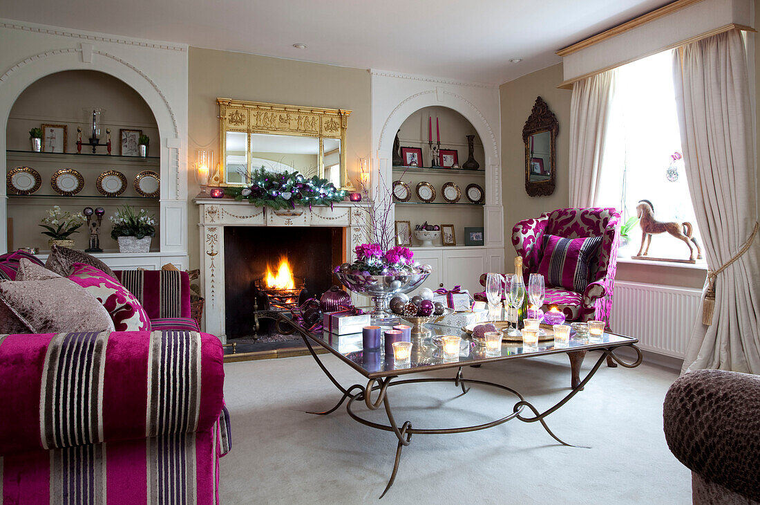 Kräftig rosa gepolstertes Sofa und Sessel im Wohnzimmer eines Bauernhauses in Surrey mit brennenden Teelichtern auf dem Couchtisch, England, UK