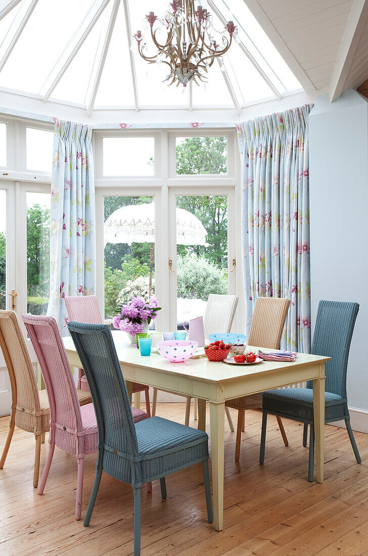 Ding room table with pastel painted chairs in conservatory of Sussex country house, England, UK