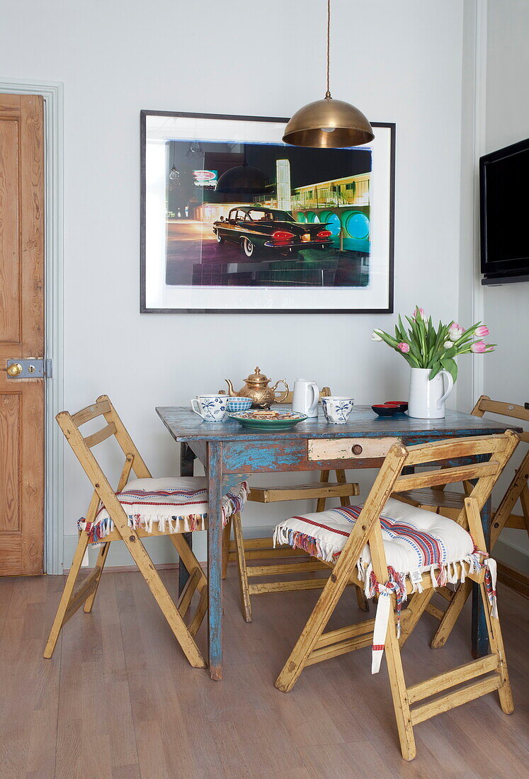 Kunstwerk mit Messing-Pendelleuchte über einem Tisch mit Holzklappstühlen in einem Londoner Haus, England, UK