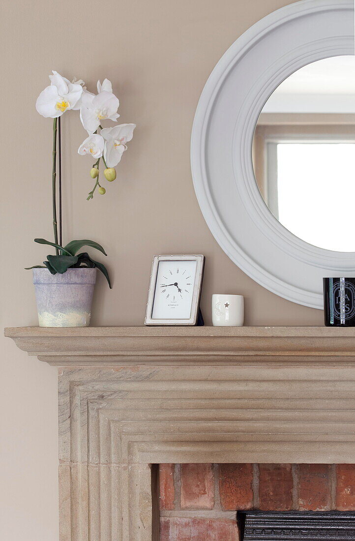 White orchid and mirror with clock on wooden mantlepiece in Staffordshire farmhouse England UK