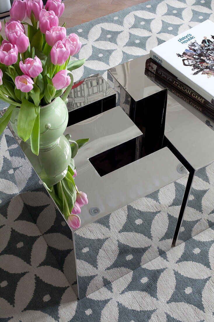 Pink tulips on mirrored coffee table with patterned rug in living room of London townhouse England UK