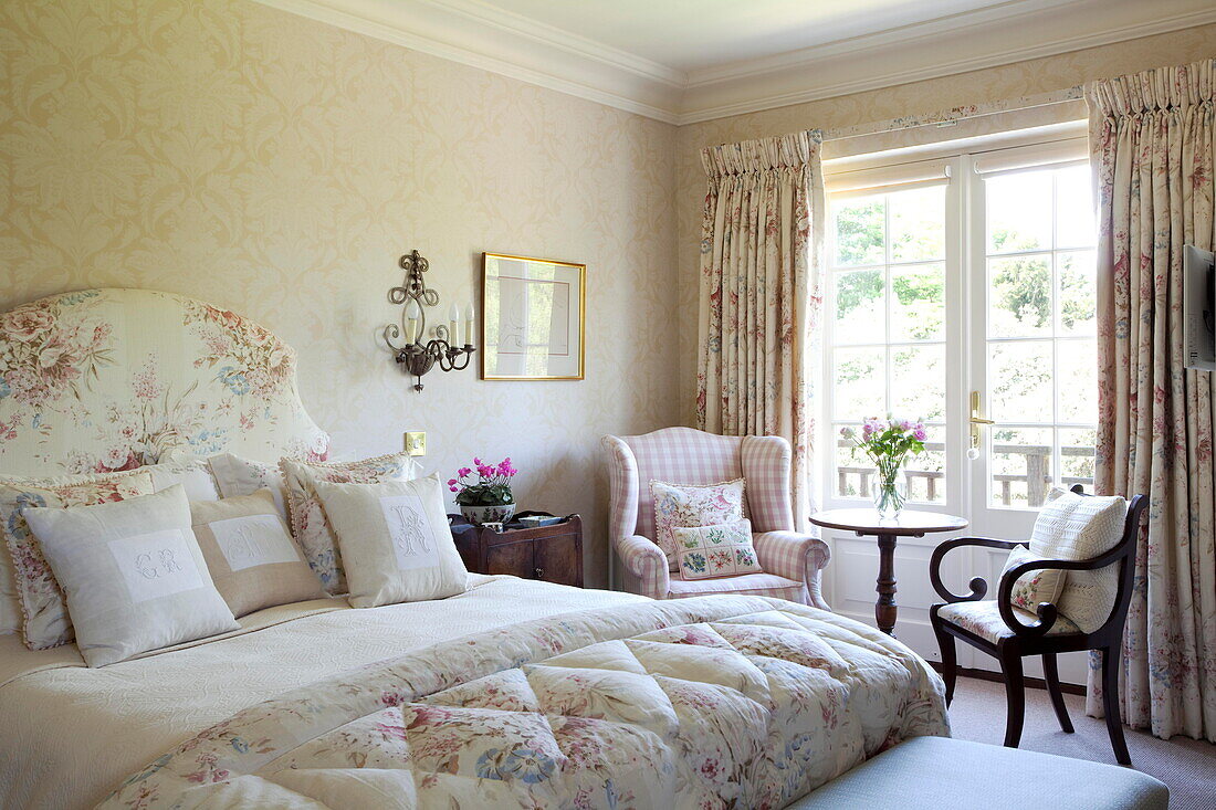 Floral curtains at window with side table in bedroom with floral patterned quilt in Kent home England UK