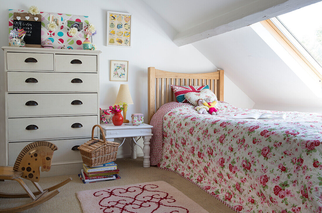 Rose patterned bedspread below dormer window in attic bedroom in Dorset cottage, England, UK