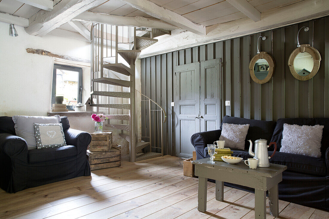 Spindeltreppe im Wohnzimmer mit schwarzen Sofas in einem bretonischen Landhaus, Westfrankreich