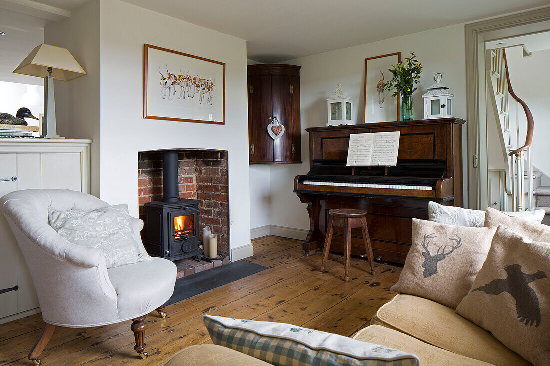 Befeuerter Kaminofen mit Klavier und Sessel im Wohnzimmer eines Hauses in Sussex Downs, England, Vereinigtes Königreich