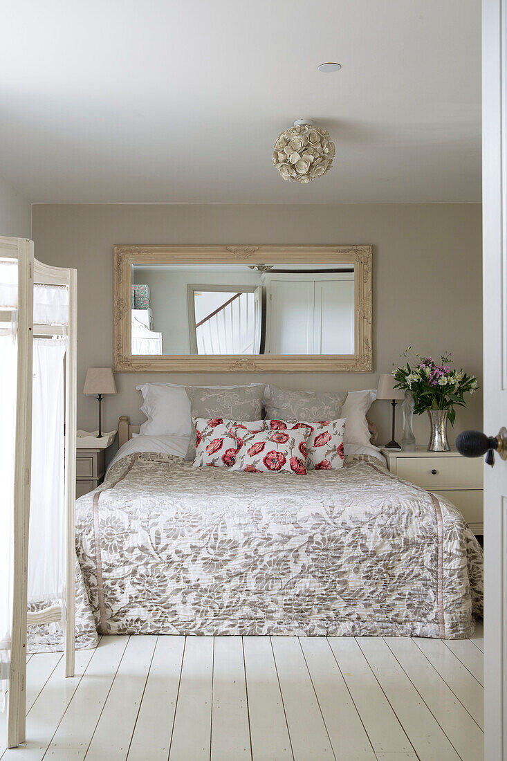 Blick durch die Tür zu einem Doppelbett unter einem rechteckigen Spiegel in einem Haus in Sussex Downs, England, UK