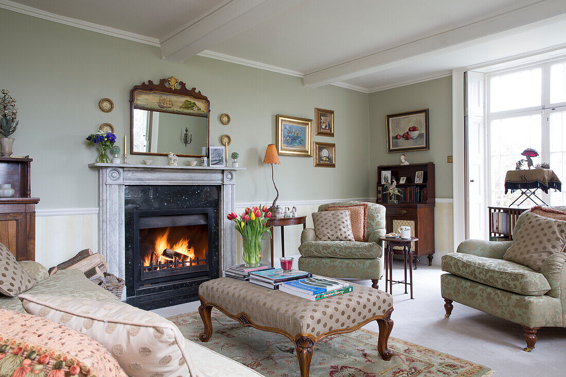 Geschnittene Tulpen auf Ottomane mit beleuchtetem Feuer im Wohnzimmer von Burwash home East Sussex England UK