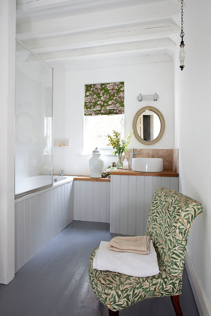 Stuhl mit Blattmuster auf einem Badezimmer mit Nut und Feder und Glasduschwand in einem Haus in West Sussex, England, UK