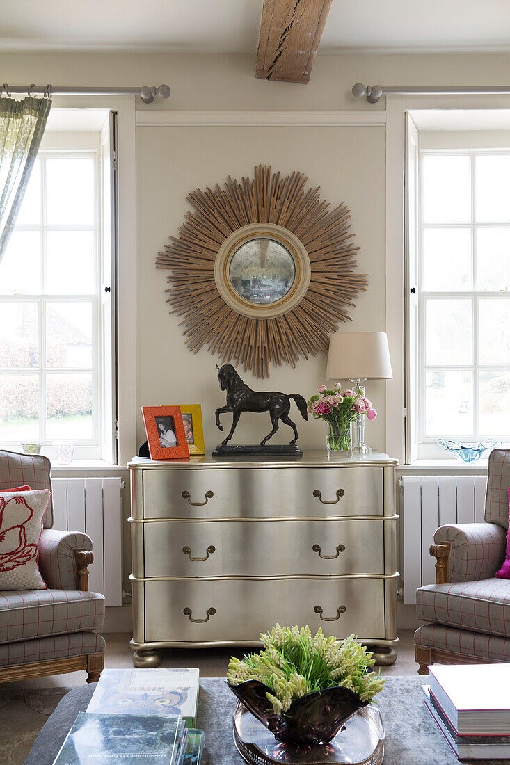 Sunburst mirror above silver chest of drawers in living room of London home England UK