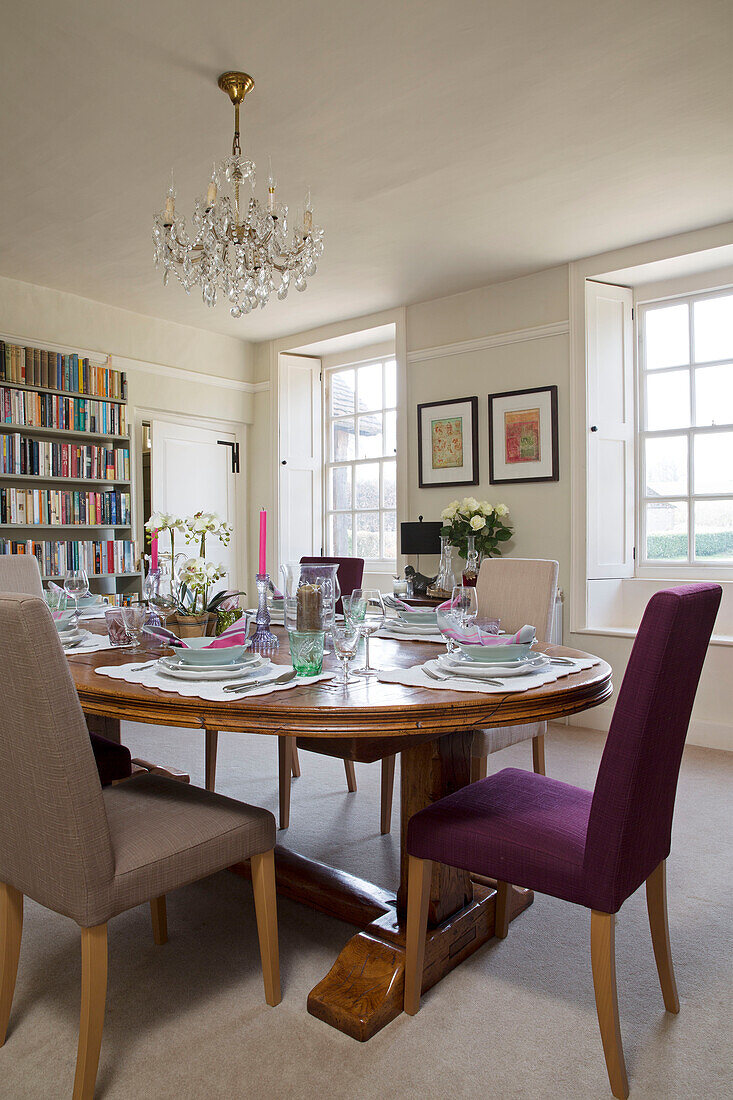 Chandelier above wooden dining table with bookshelves in London home England UK