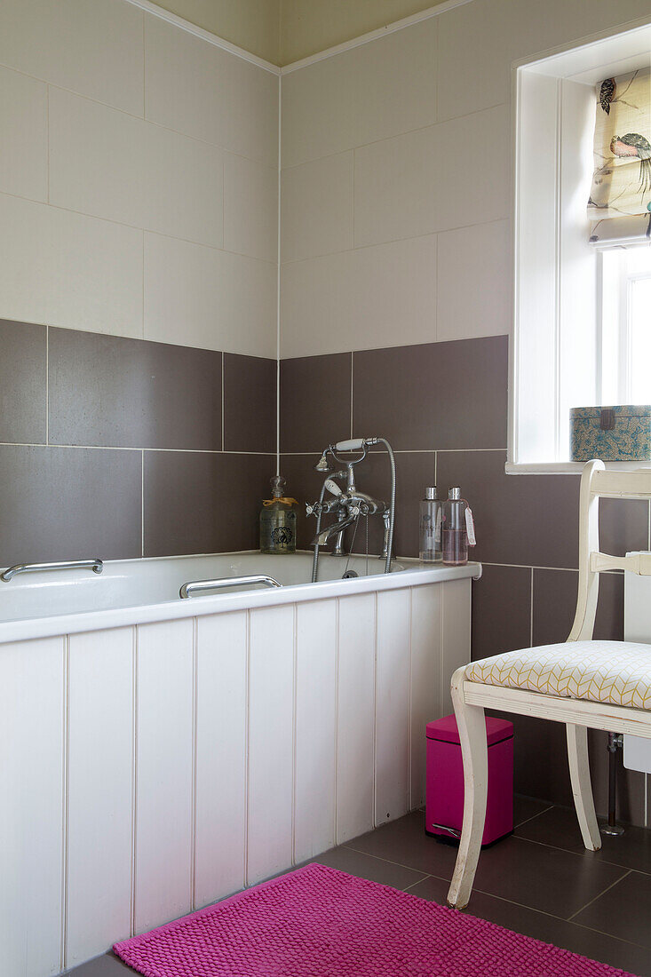 Tongue and groove bath with brown tiling and pink bathmat in London home England UK